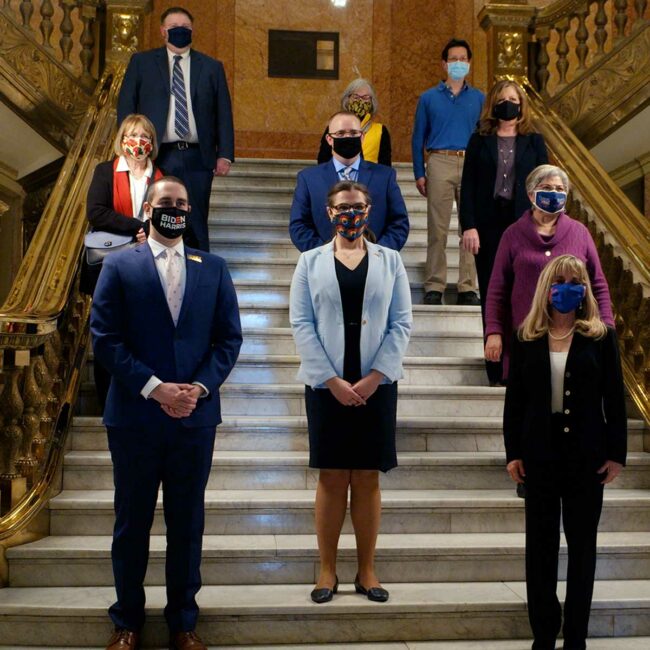 Colorado 2020 Electors with CO Secretary of State, Jena Griswold, they are all wearing protective face masks and stand on the steps of the capitol in Denver.